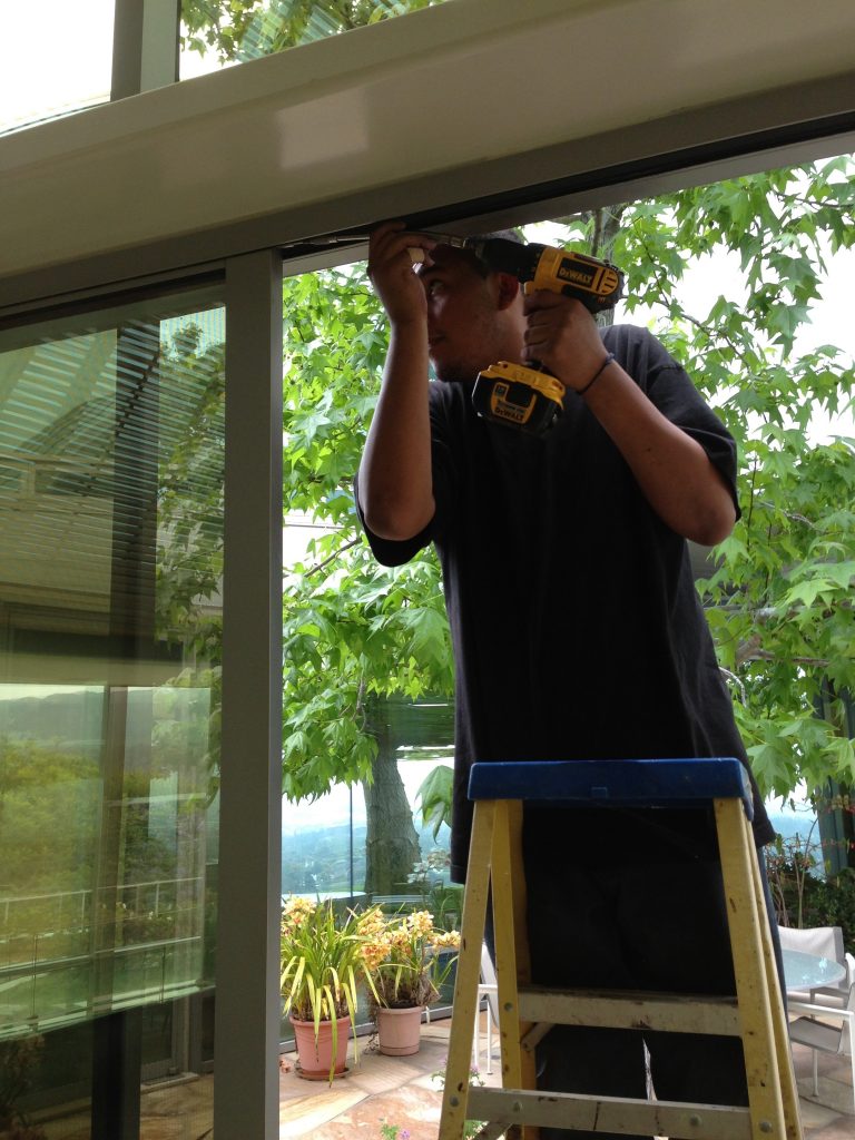 One of our techs standing on a ladder and fixing the track of a broken sliding door